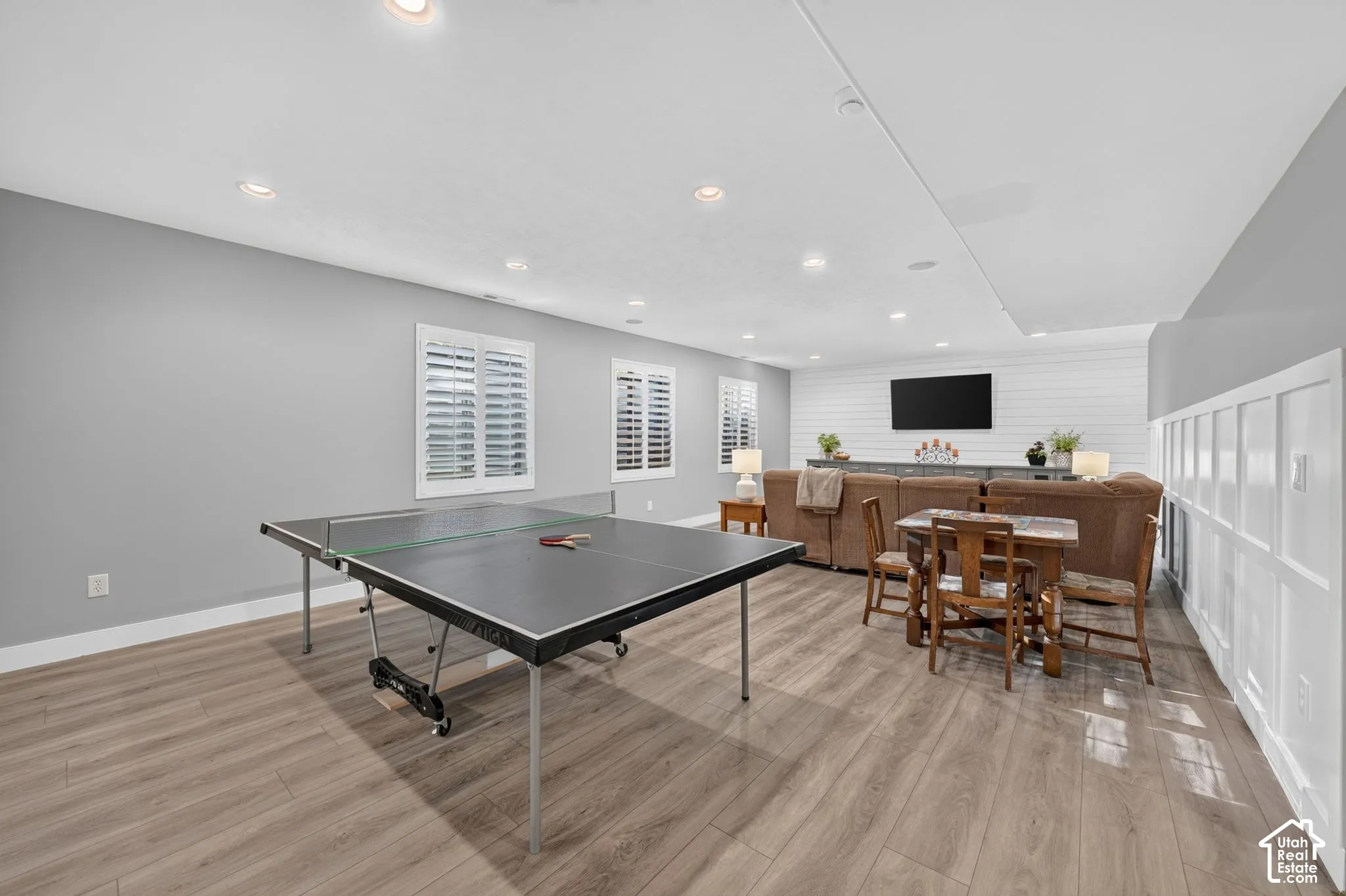 Spacious room featuring wood-finish flooring, recessed lighting, horizontal shiplap wall accent, board-and-batten wainscoting, and plantation shutters