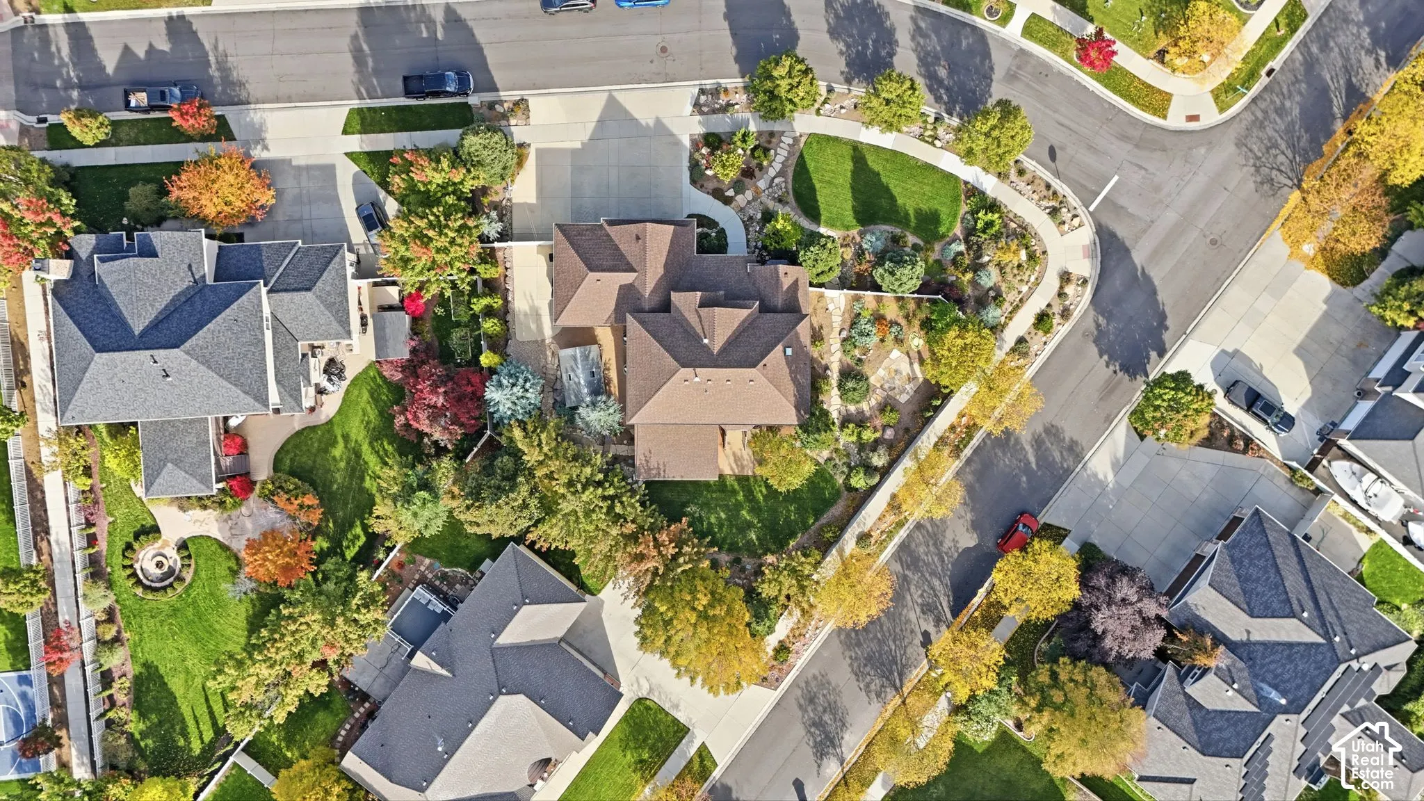 Aerial perspective featuring a corner lot, multi-faceted shingle roof, paved driveway, landscaped grounds, and mature trees