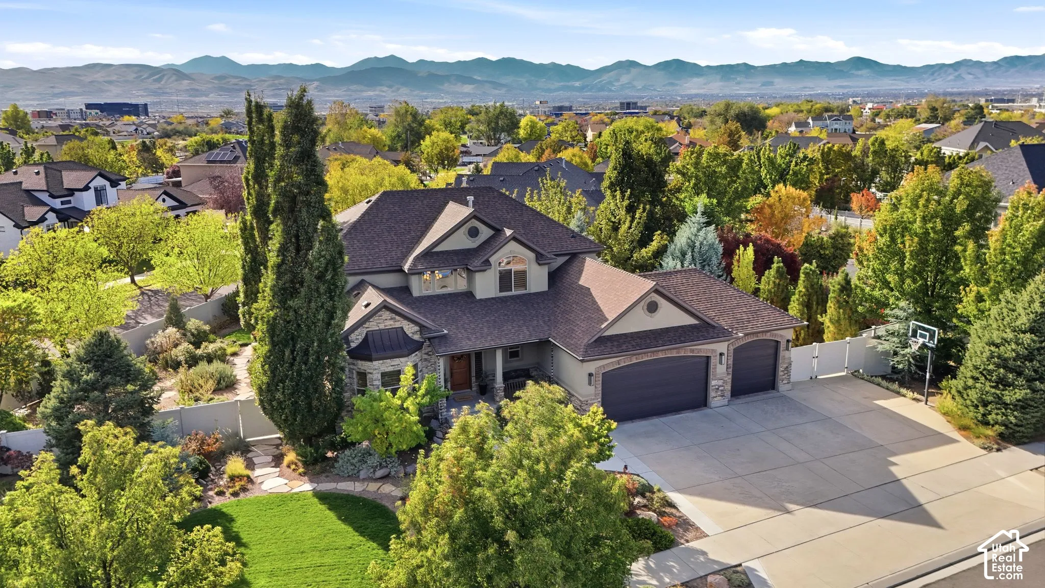 Two-story residence featuring a multi-gabled roofline, stone and stucco exterior, three-car garage, concrete driveway, and expansive mountain scenery