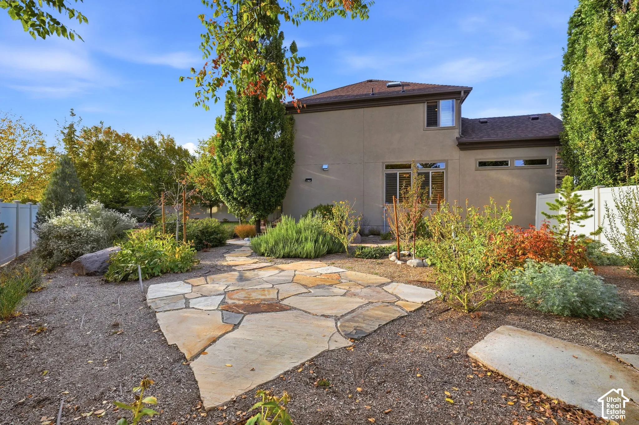 Stucco exterior with a multi-level roofline, featuring a flagstone patio, gravel landscaping, and mature shrubbery