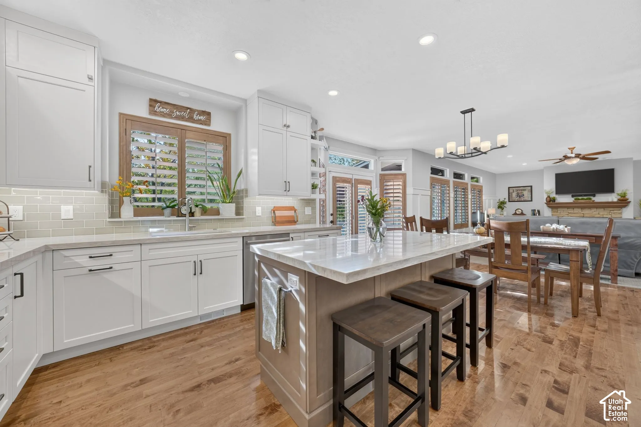 Kitchen featuring white shaker-style cabinetry, light-toned stone countertops, a central island with wood-finish cabinetry, subway tile backsplash, and recessed lighting