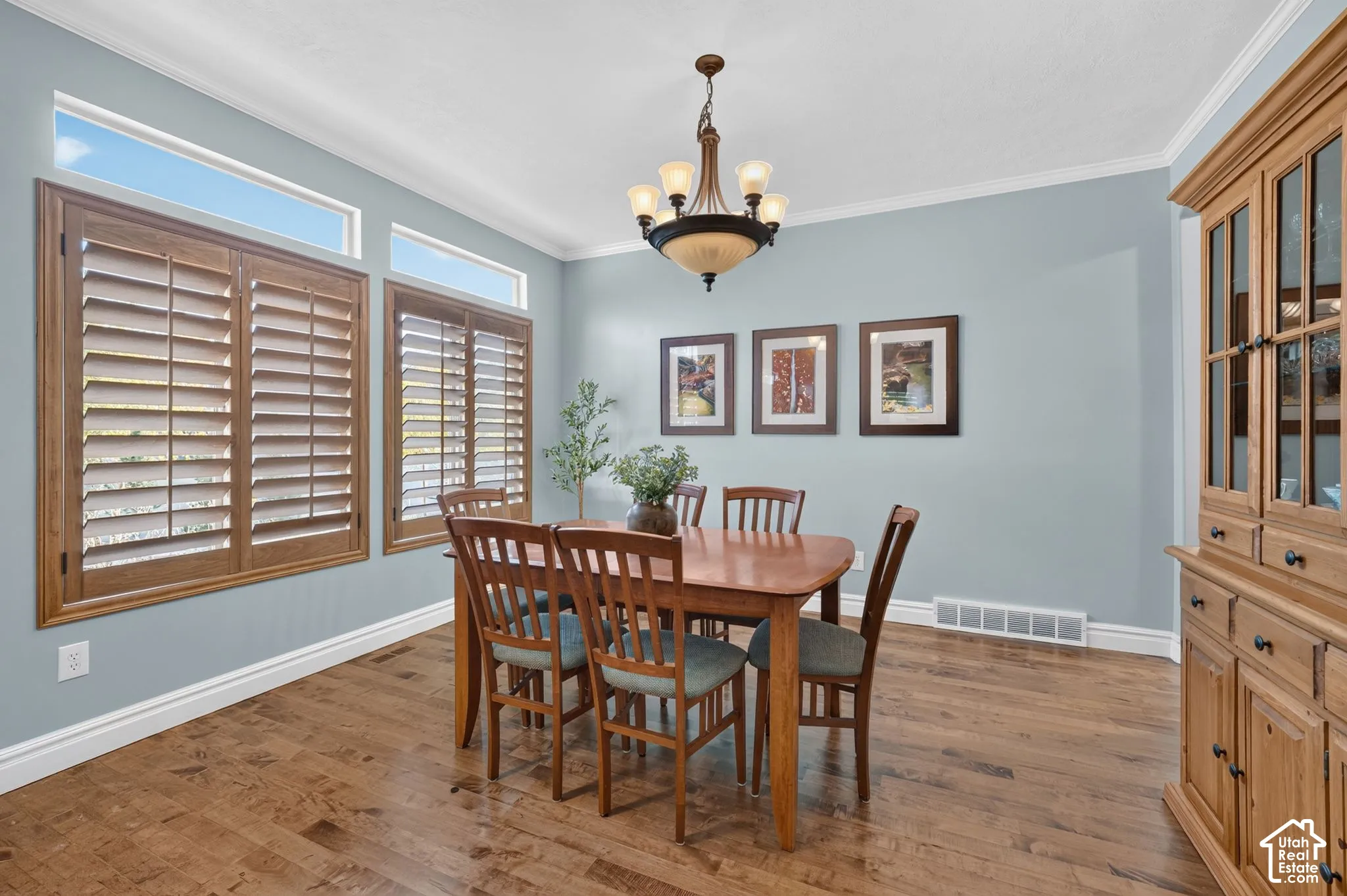 Wood-finish flooring, plantation shutters, crown molding, tiered chandelier, and built-in wood cabinetry