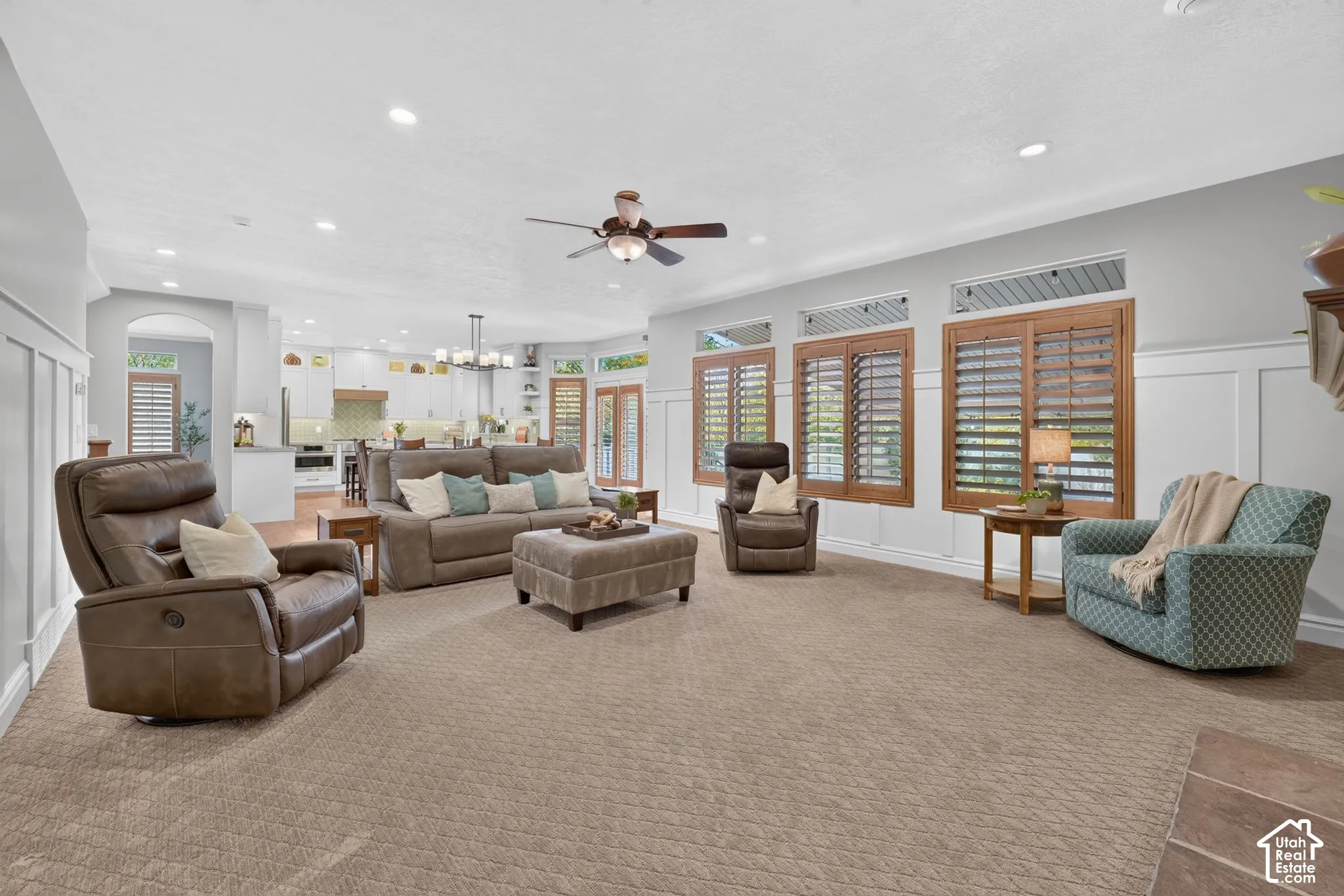 Spacious living area featuring white wainscoting, recessed lighting, a ceiling fan, and large windows with wooden plantation shutters