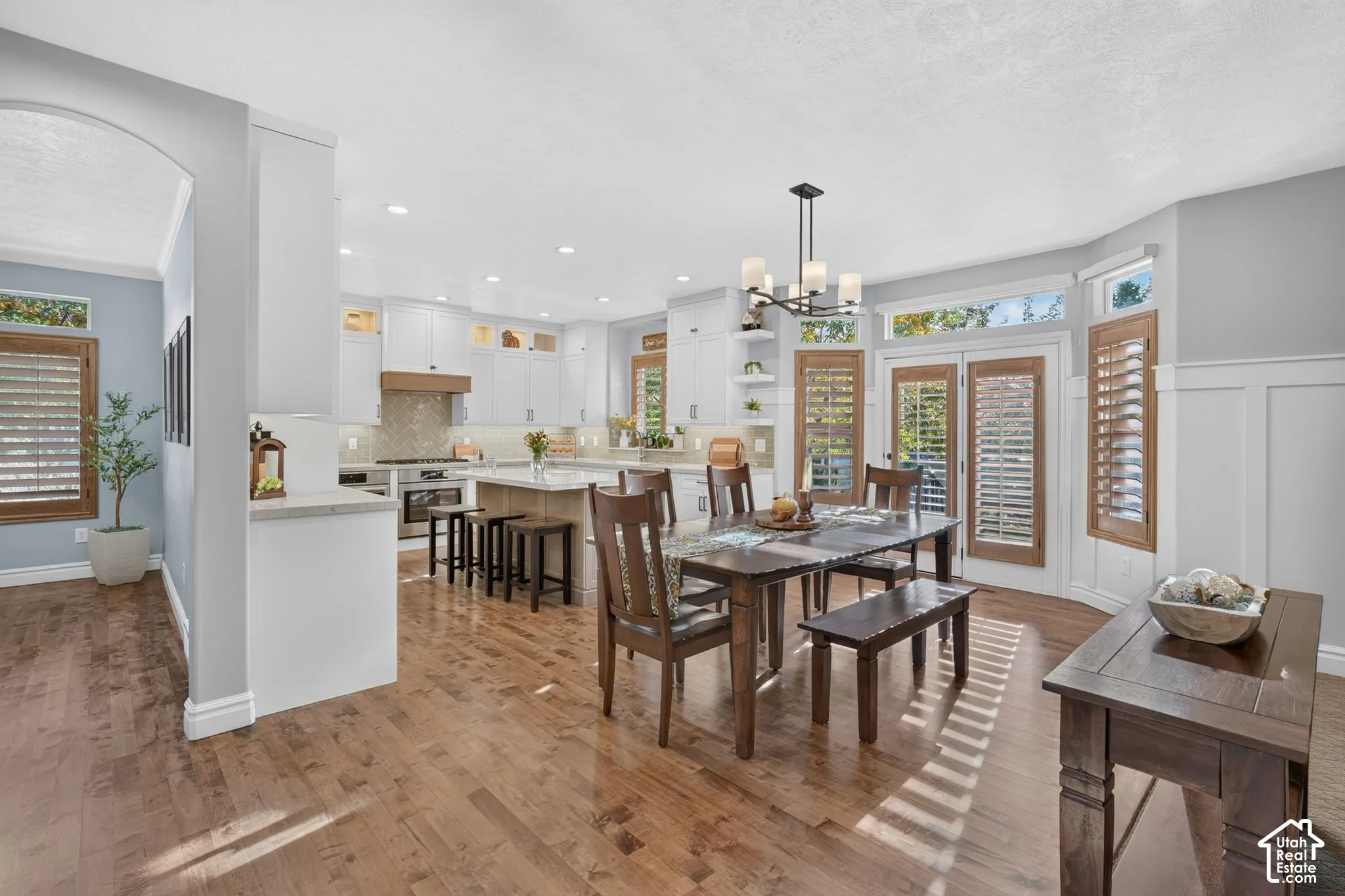 Open-concept kitchen featuring shaker-style cabinetry, an expansive center island with stone-finish countertops, wood-finish flooring, wainscoting detail, and transom windows
