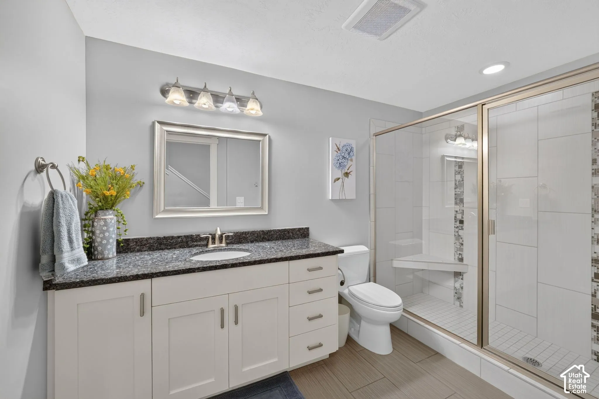 Bathroom featuring a stone-top vanity with built-in cabinetry, a walk-in shower with a glass enclosure and built-in bench, tile flooring, and a multi-light fixture