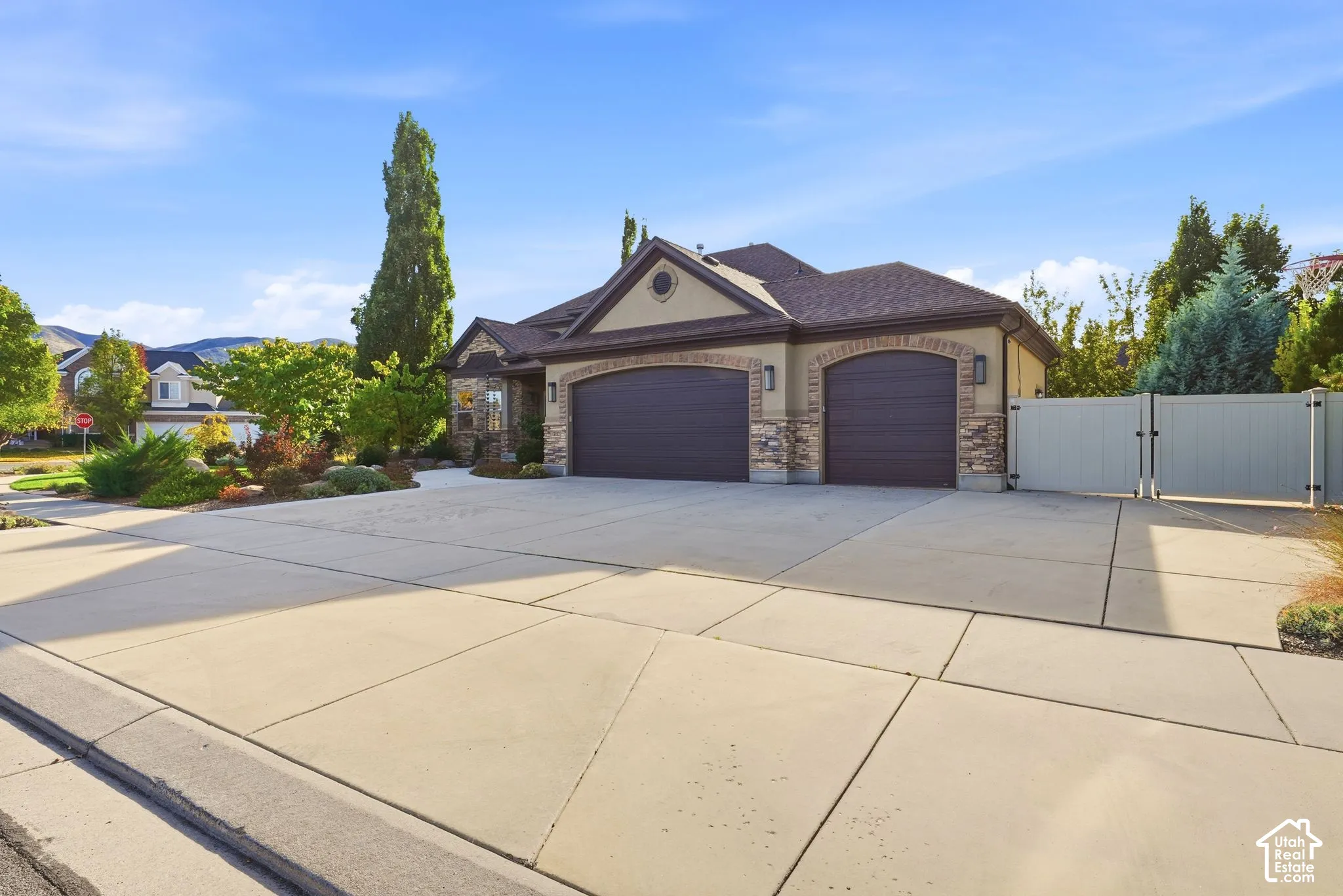 Exterior facade featuring stone veneer detailing, a multi-car garage, concrete driveway, and solid panel fencing