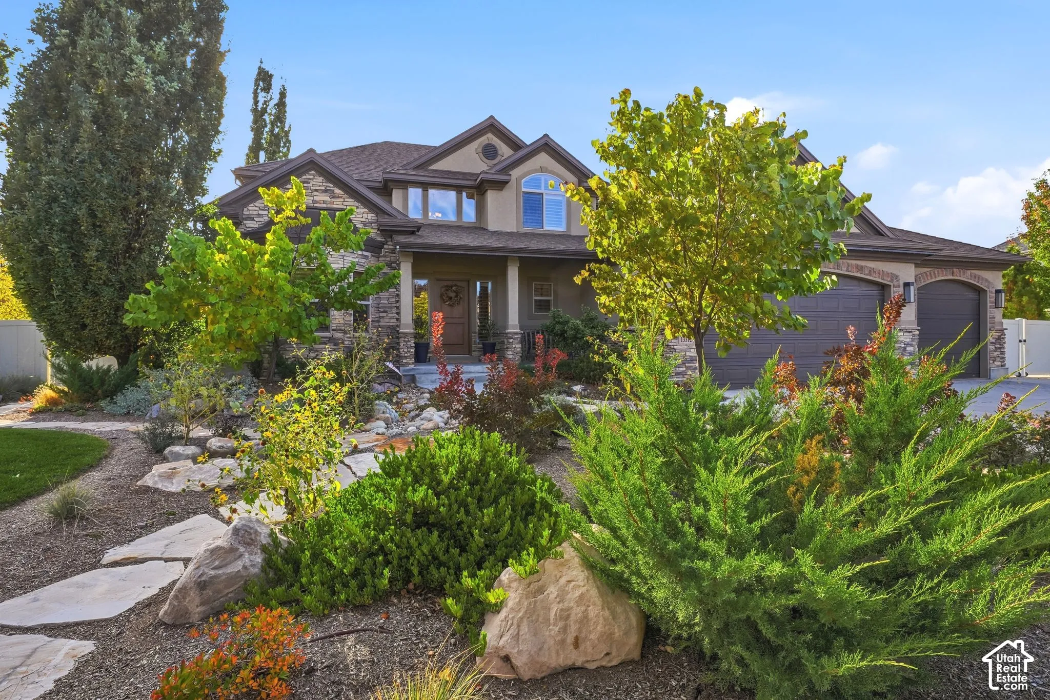 Exterior facade featuring stone and stucco siding, a multi-gabled roofline, arched garage bays, and a covered entry, set within a landscaped yard with stone pathways