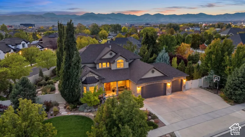 Multi-level residence featuring stone and stucco exterior, three-car garage, concrete driveway, stone-paved walkway, and manicured landscaping set against a mountain backdrop