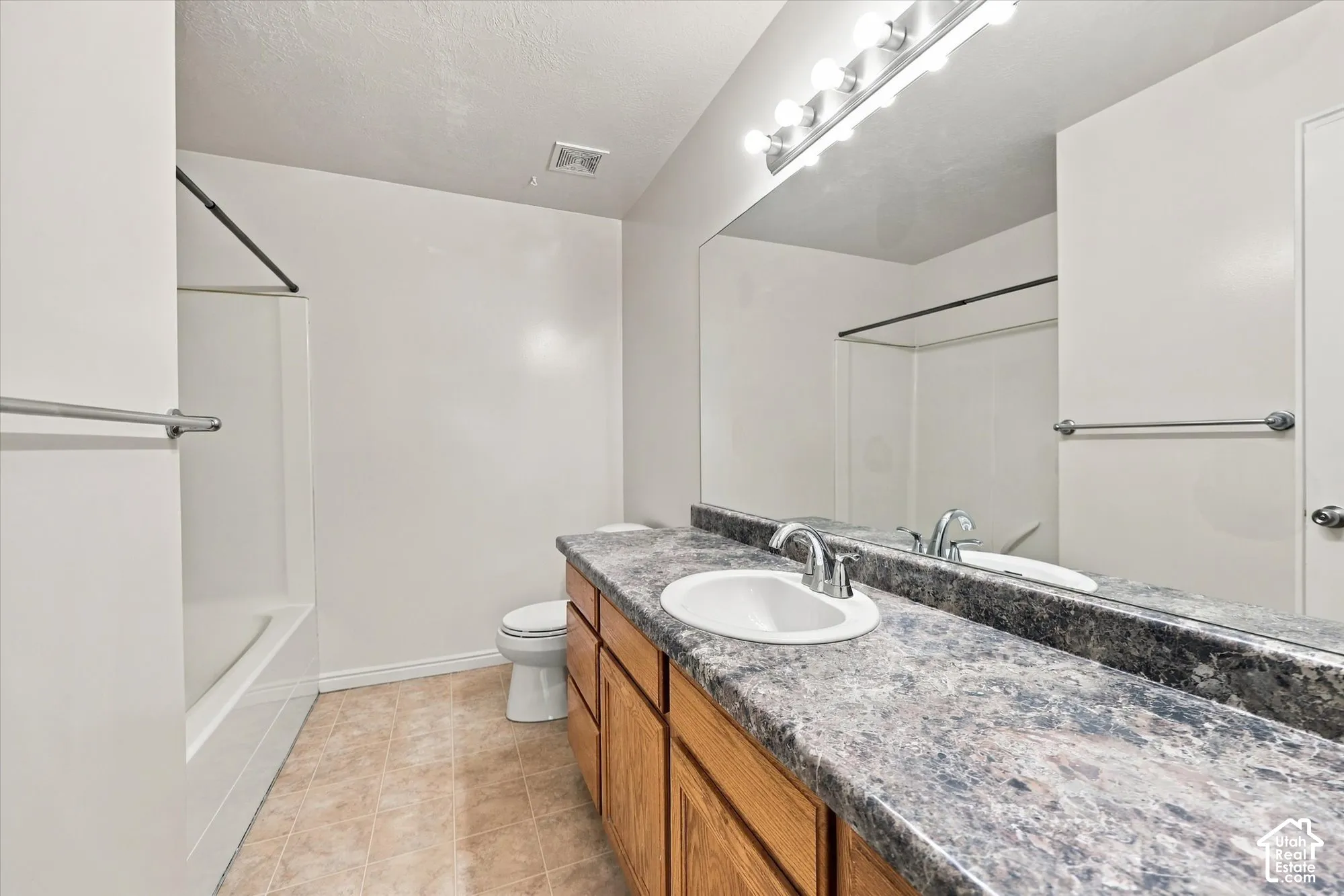 Bathroom featuring a vanity with stone-finish countertop, integrated sink, wood-finish cabinetry, full-width mirror, and a combined tub and shower enclosure