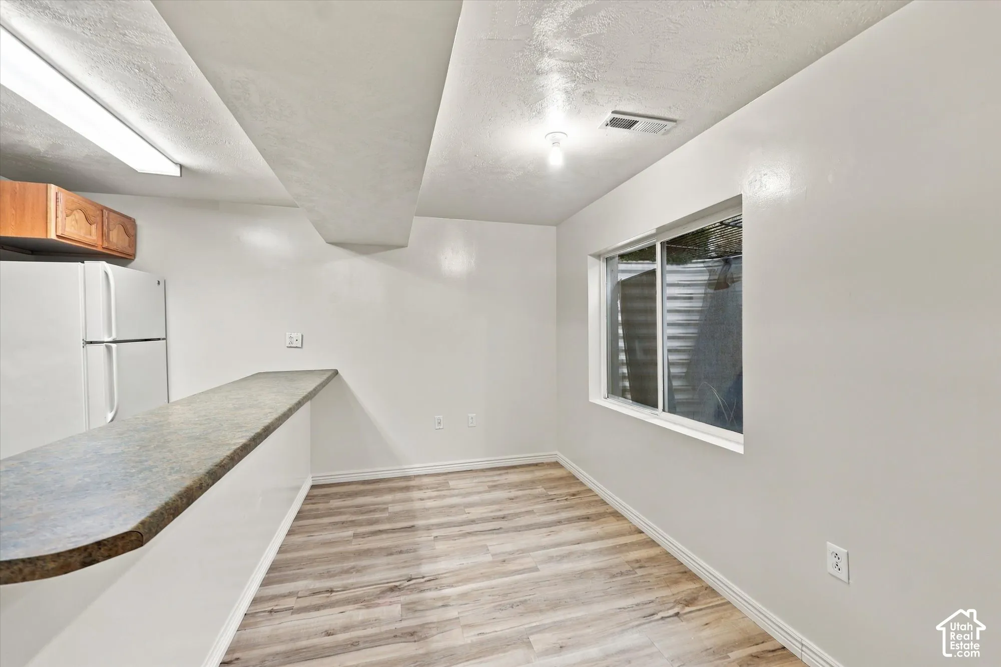 Wood-finish flooring, breakfast bar with solid-surface countertop, ceiling-mounted light fixture, and window with exterior window well