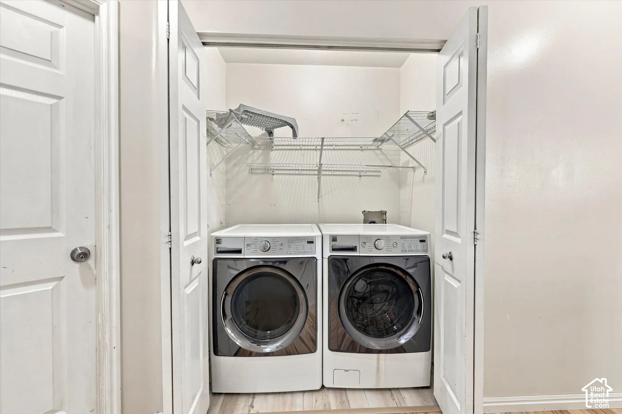 Laundry nook featuring bi-fold doors, white front-loading appliances, and tiered wire shelving