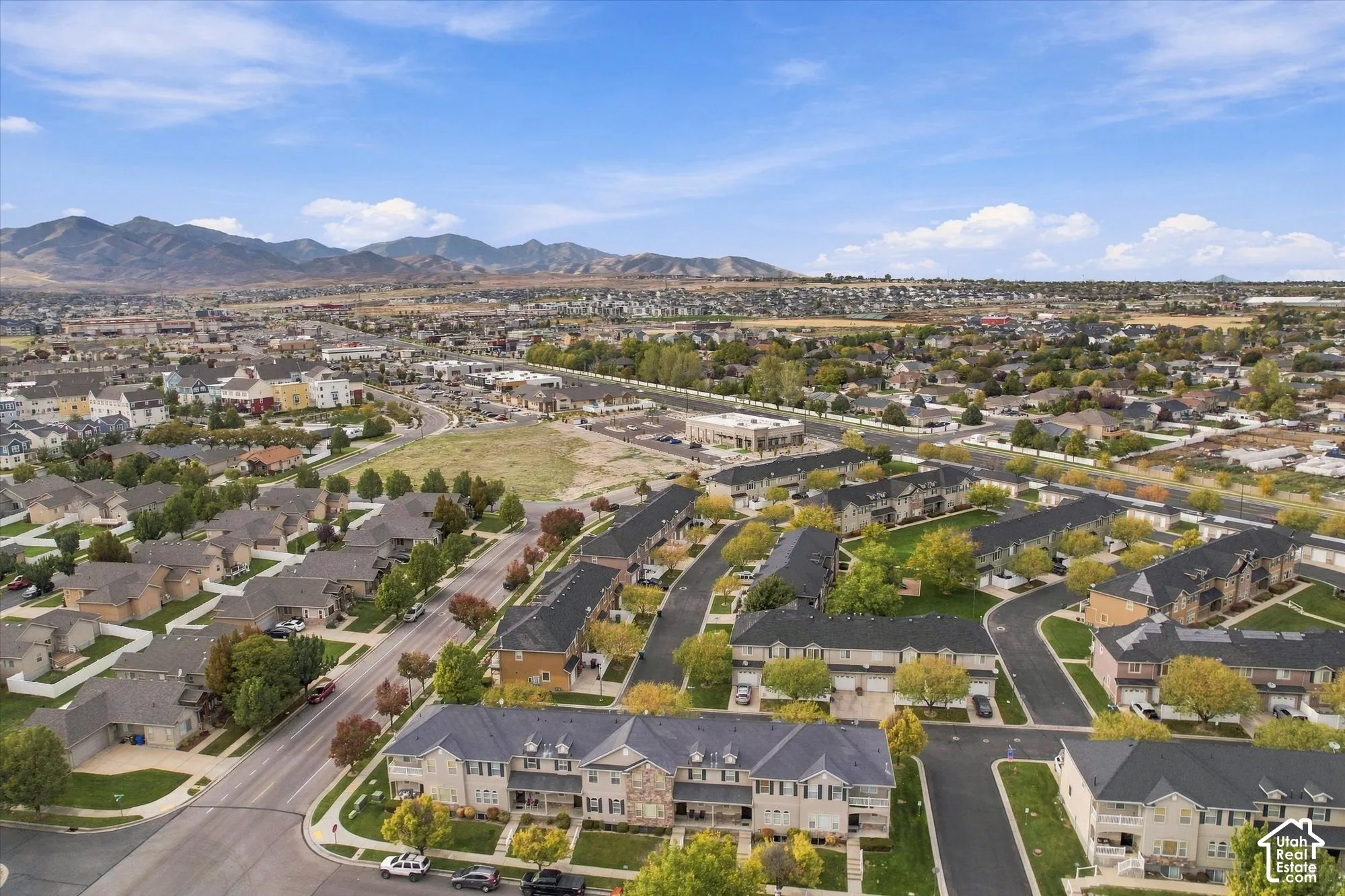 Aerial perspective of a multi-unit residential community featuring asphalt roadways, brick and composite siding exteriors, dark-toned shingle roofing, and a mountain range backdrop