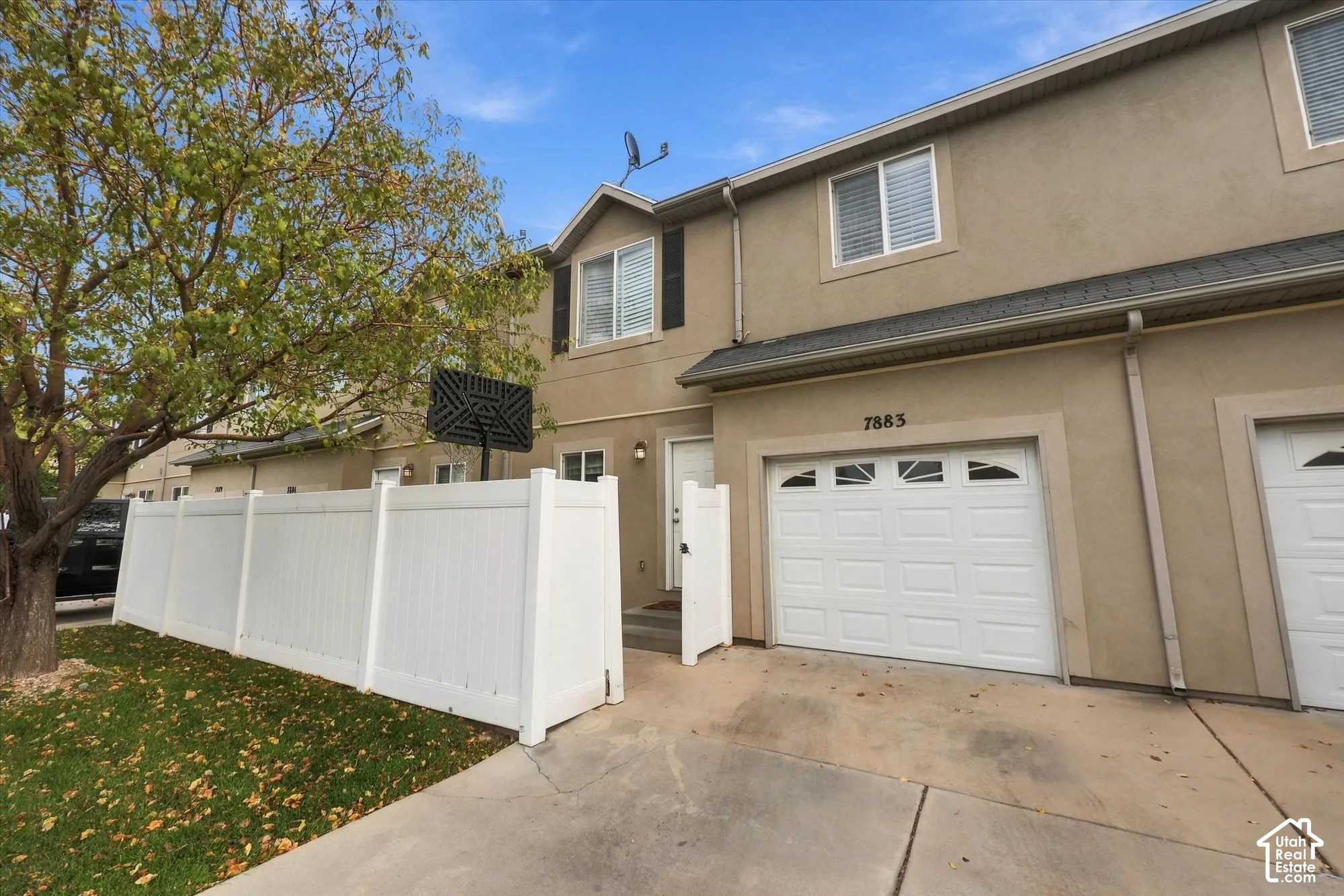 Two-story townhome exterior featuring a stucco facade, attached single-car garage with an arched-top window, white vinyl privacy fencing, and a concrete driveway
