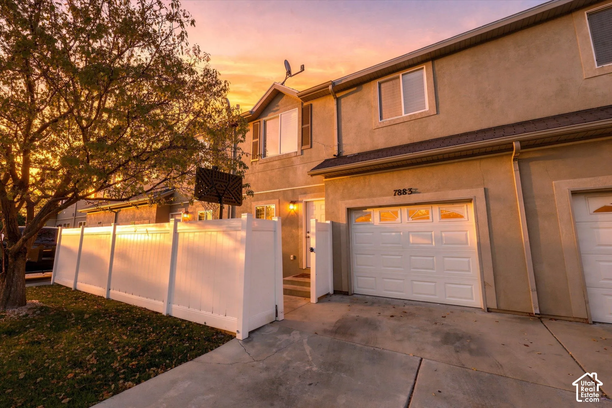 Multi-level exterior featuring a stucco facade, private white vinyl privacy fencing, integrated garage, and concrete driveway