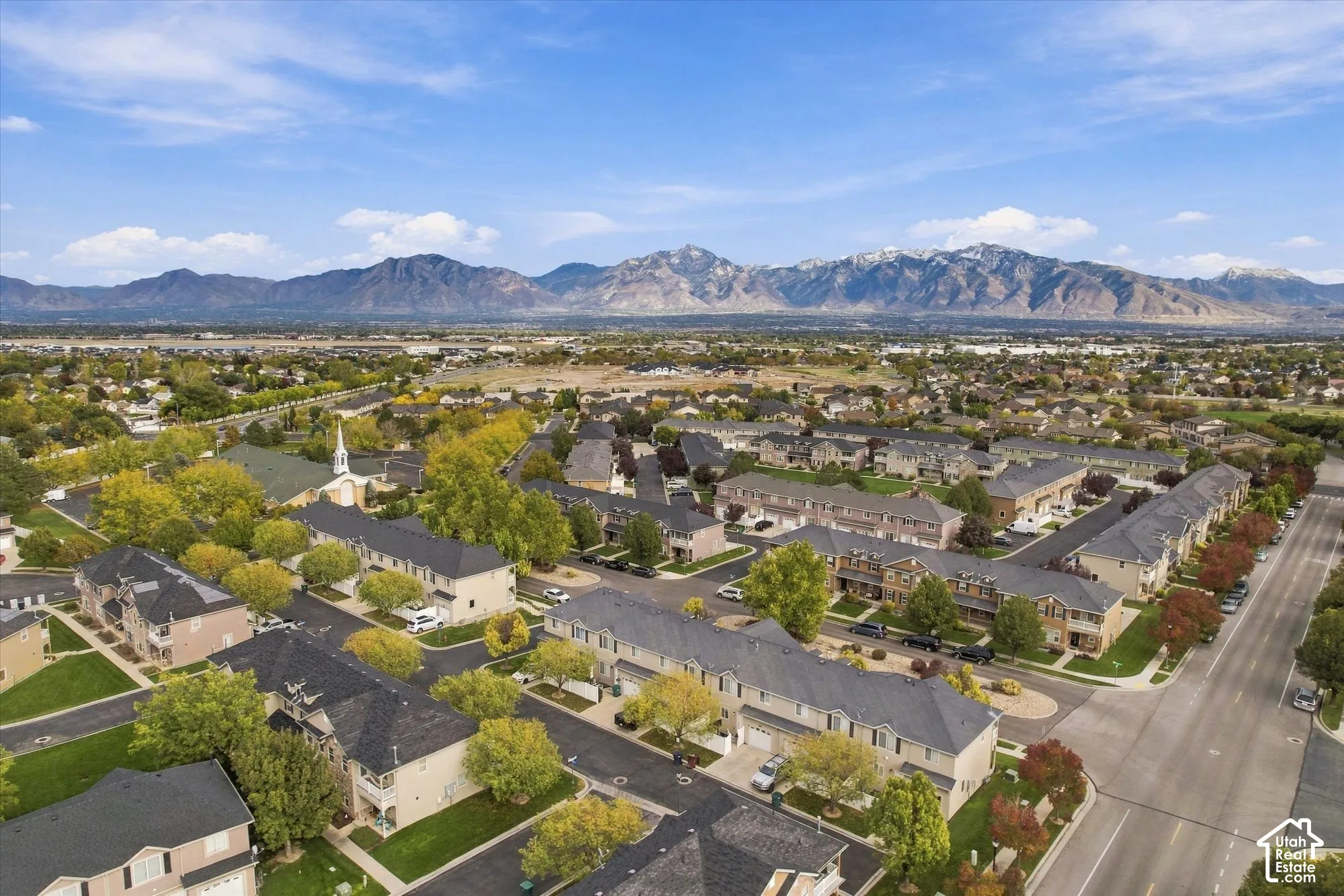 Aerial perspective of a multi-unit residential community featuring asphalt-shingle roofing, paved roads, and mature trees with a prominent mountain range backdrop
