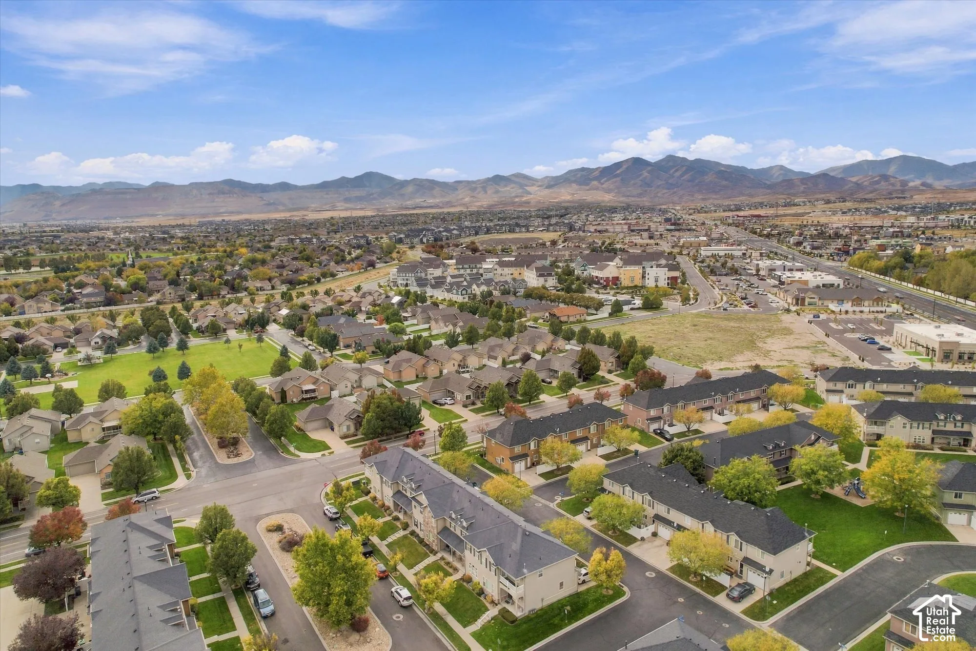 Aerial perspective featuring a multi-unit residential community with paved roadways, managed green spaces, and a mountainous horizon