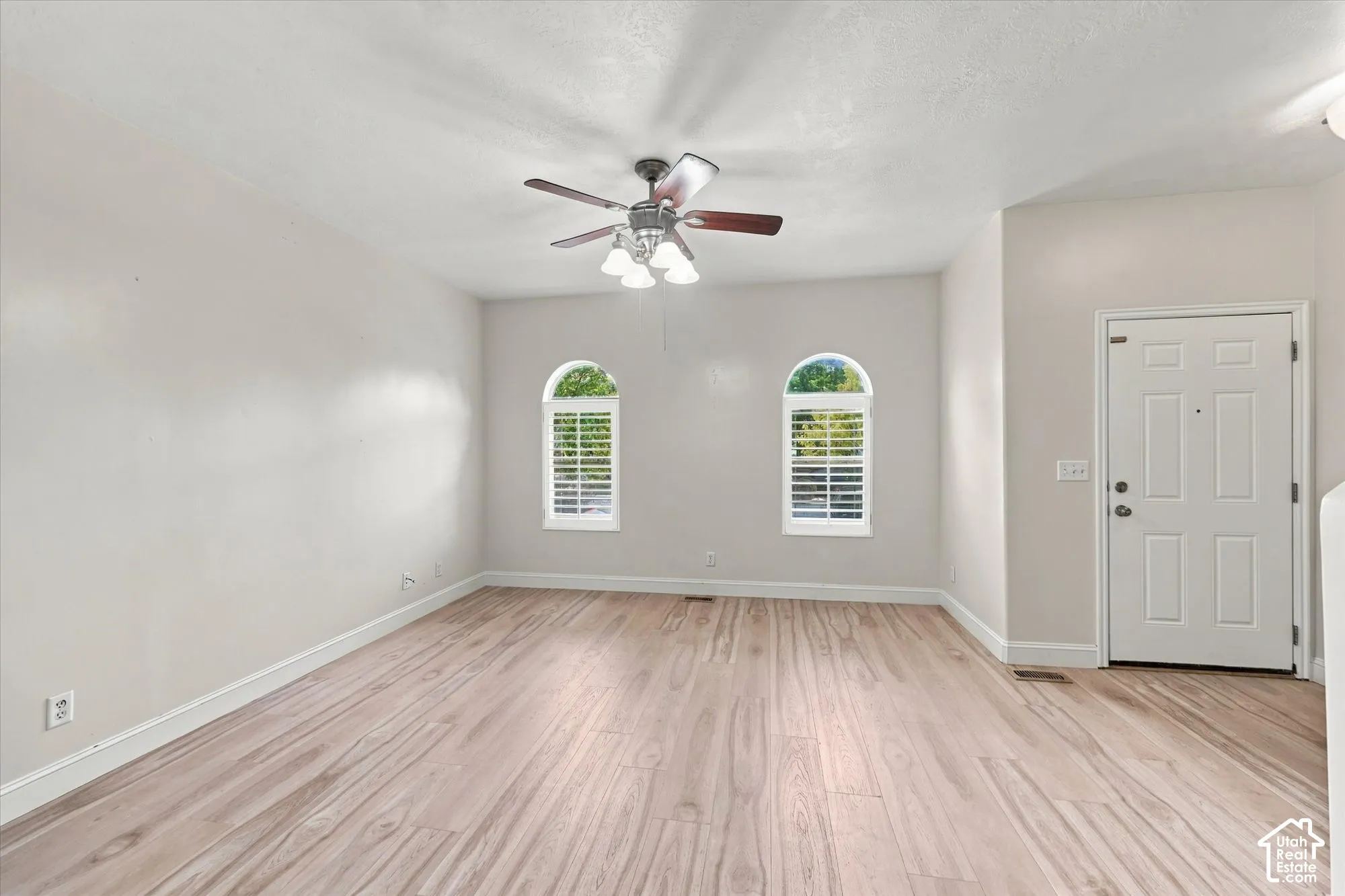 Interior space featuring wood-finish flooring, two arched windows with shutter treatments, and a ceiling-mounted fan with integrated light fixture