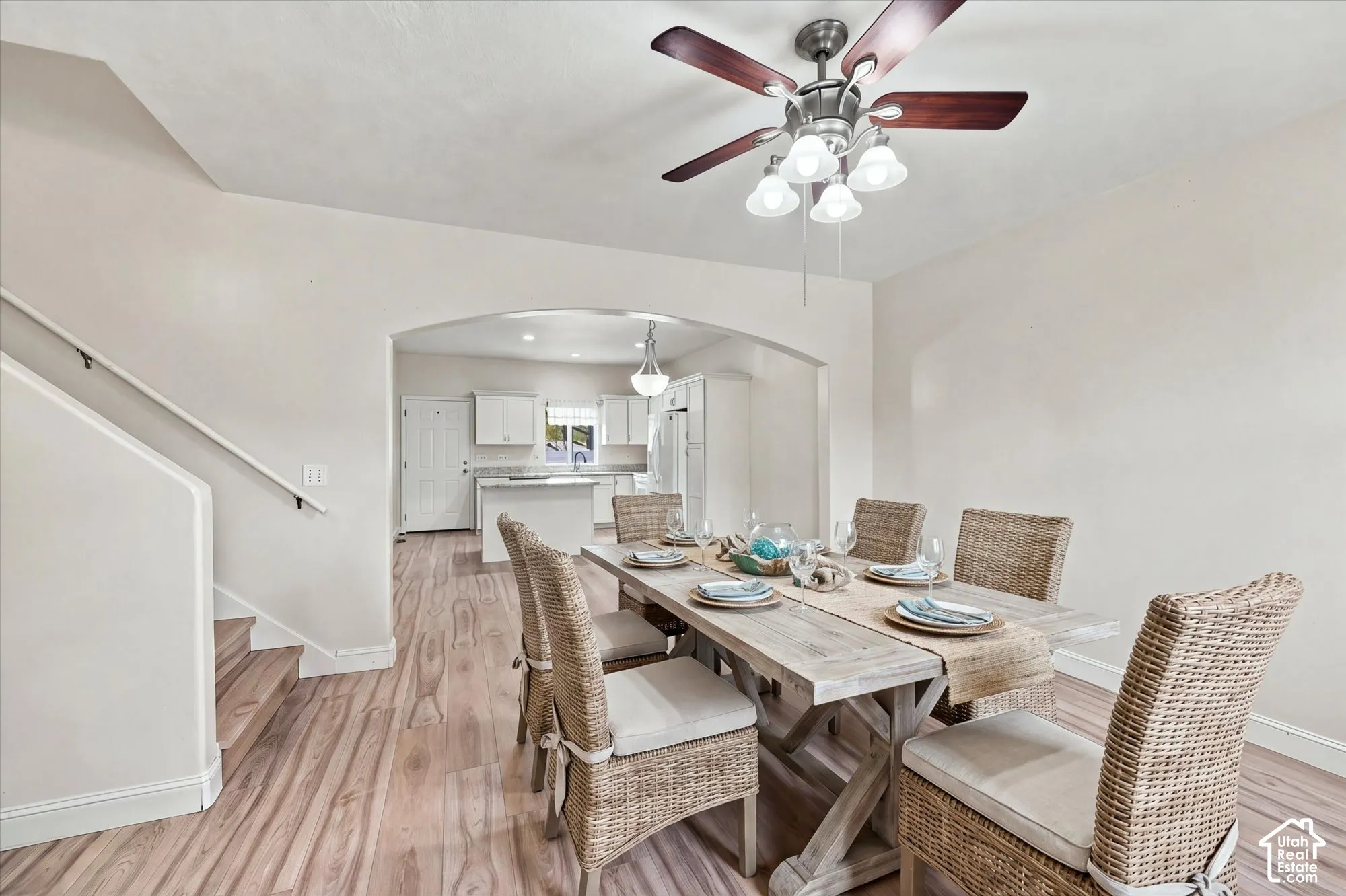 Wood-finish flooring, architectural arched opening, ceiling fan with integrated multi-bulb light fixture, and white cabinetry