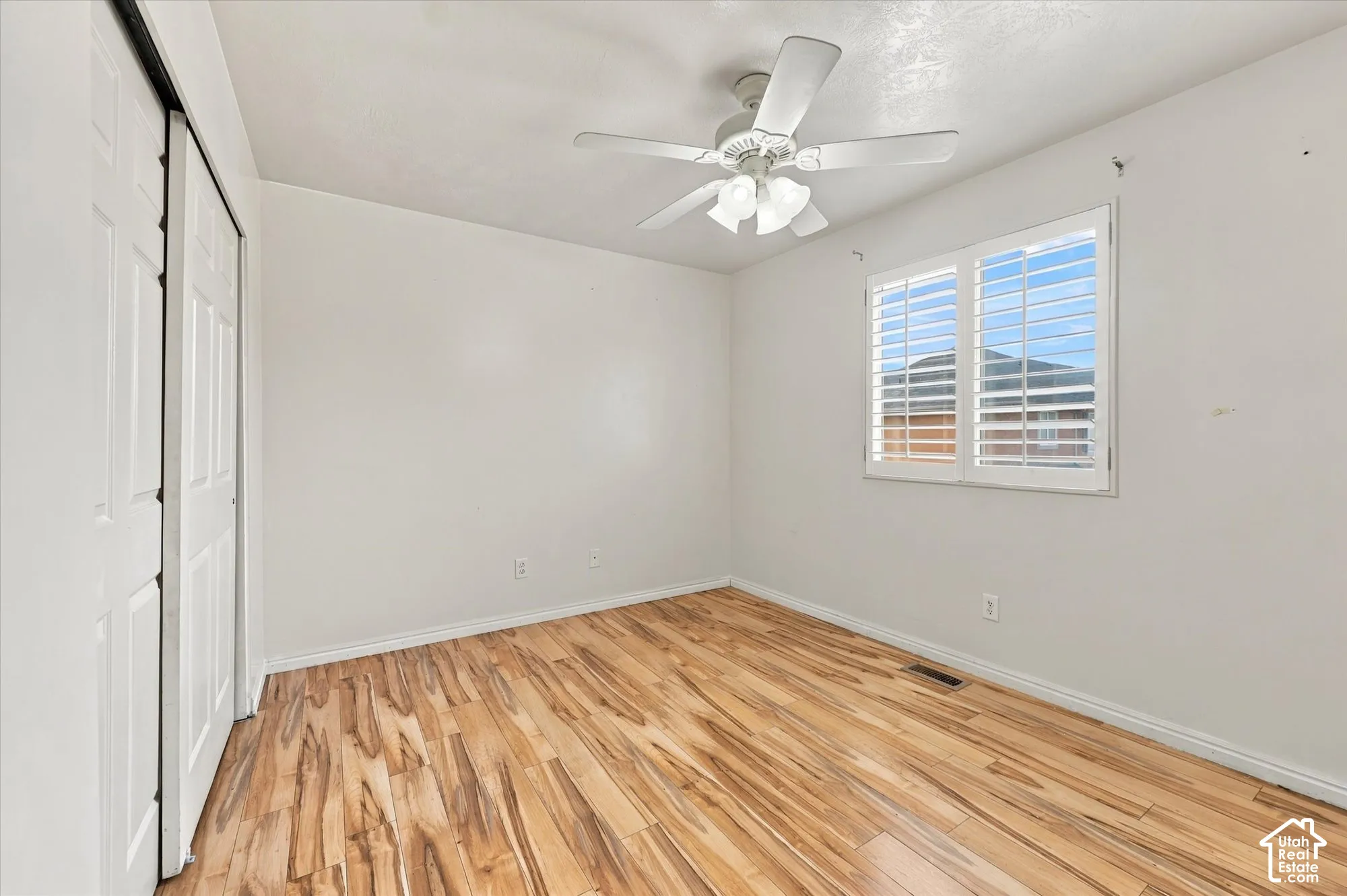 Wood-finish flooring, white plantation shutters, dual-panel sliding closet doors, and a ceiling-mounted light fixture with a fan