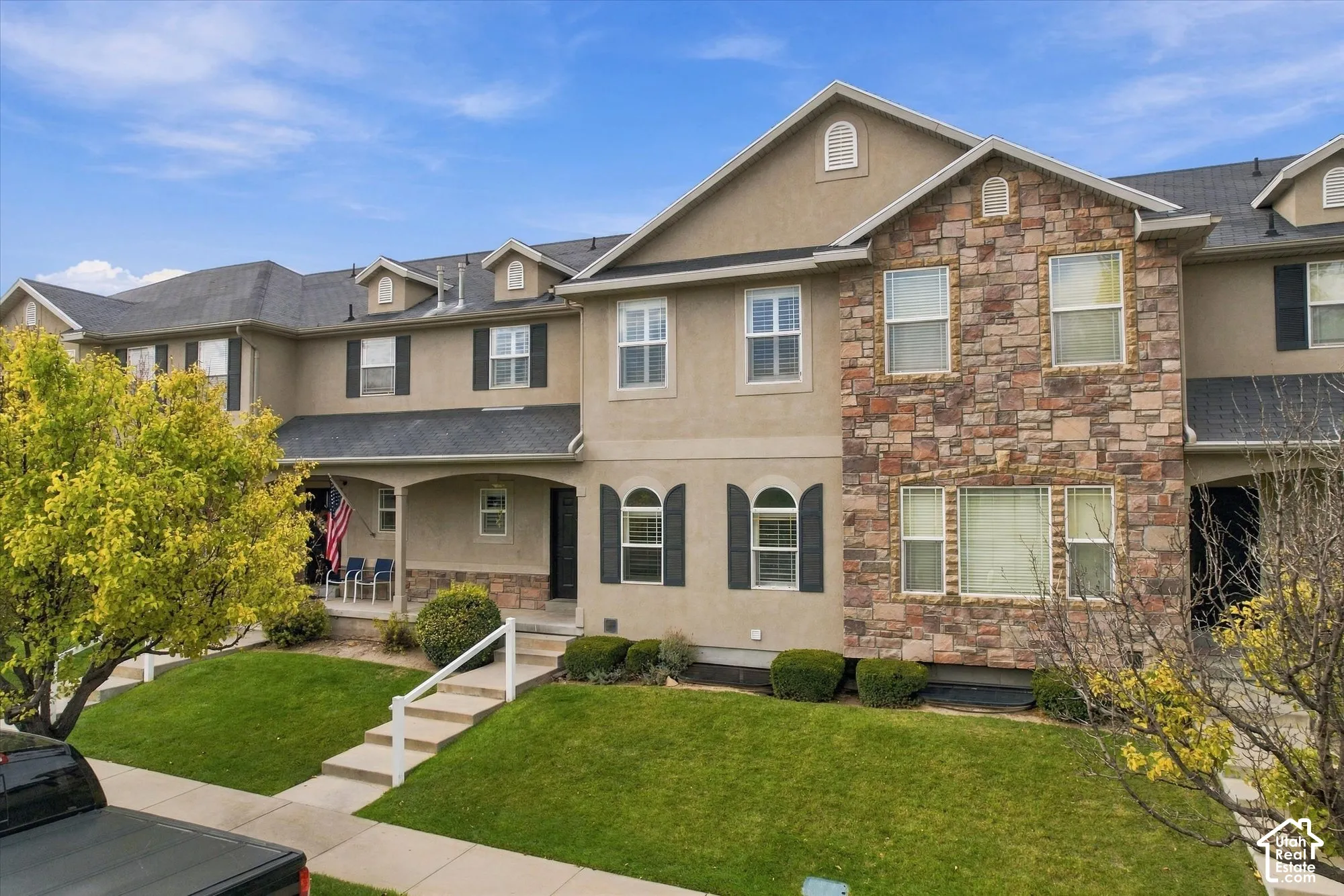 Multi-level exterior featuring stucco siding, stone veneer accents, arched window detailing, shuttered windows, and a covered front porch