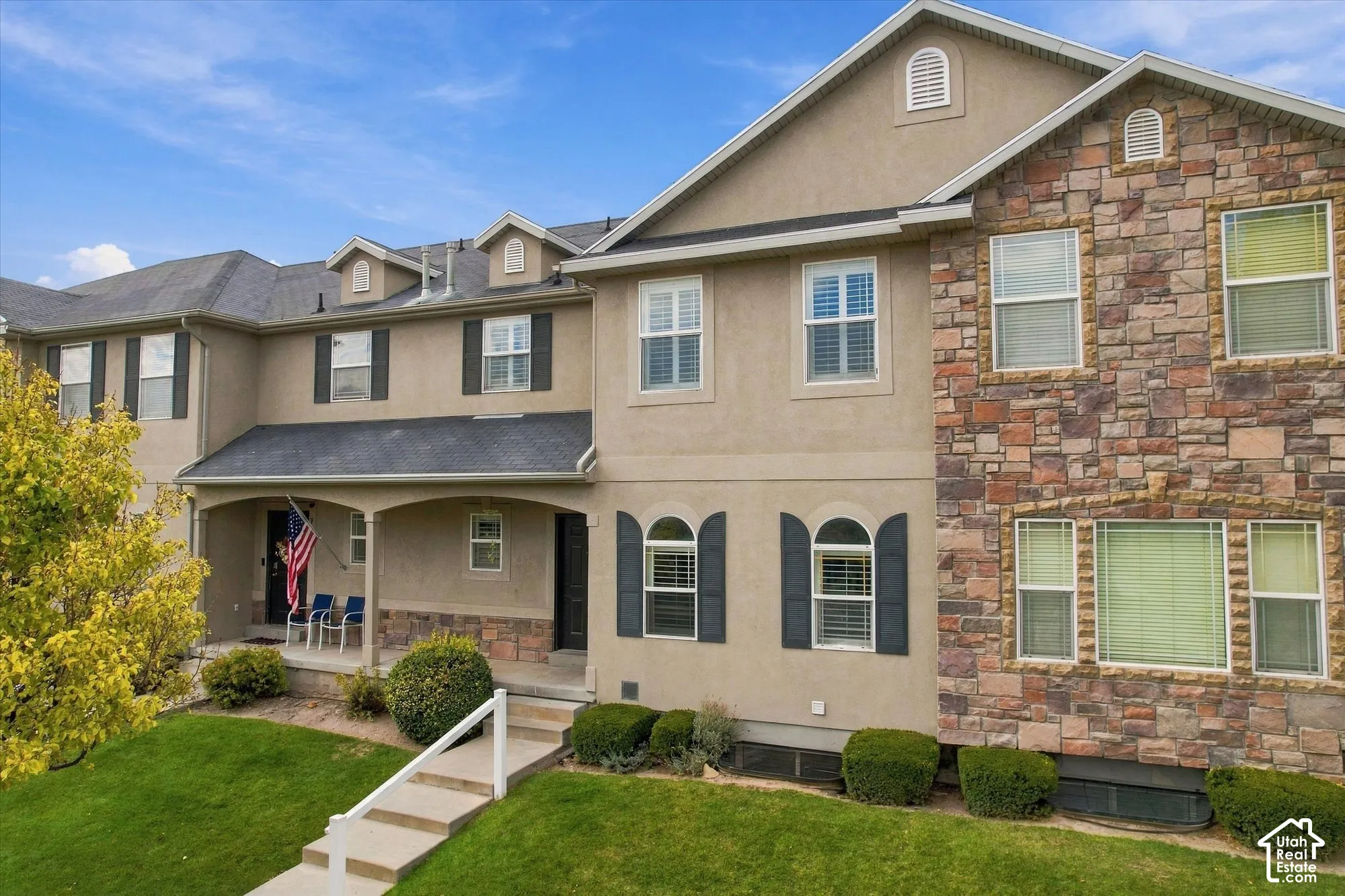 Multi-story exterior featuring a stone veneer facade, stucco siding, arched window accents, shutter detailing, and a covered front porch
