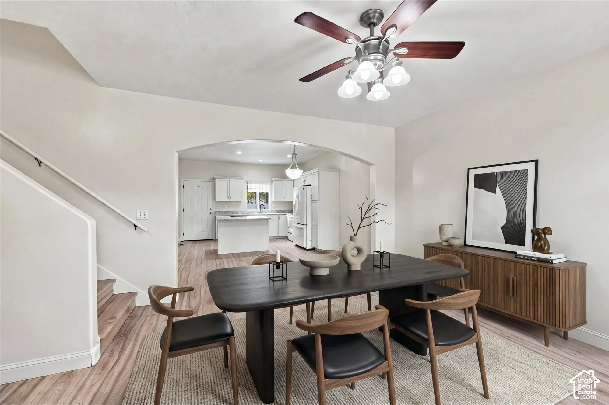 Wood-finish flooring, architectural arched wall opening, multi-blade ceiling fan with integrated lighting, and white cabinetry