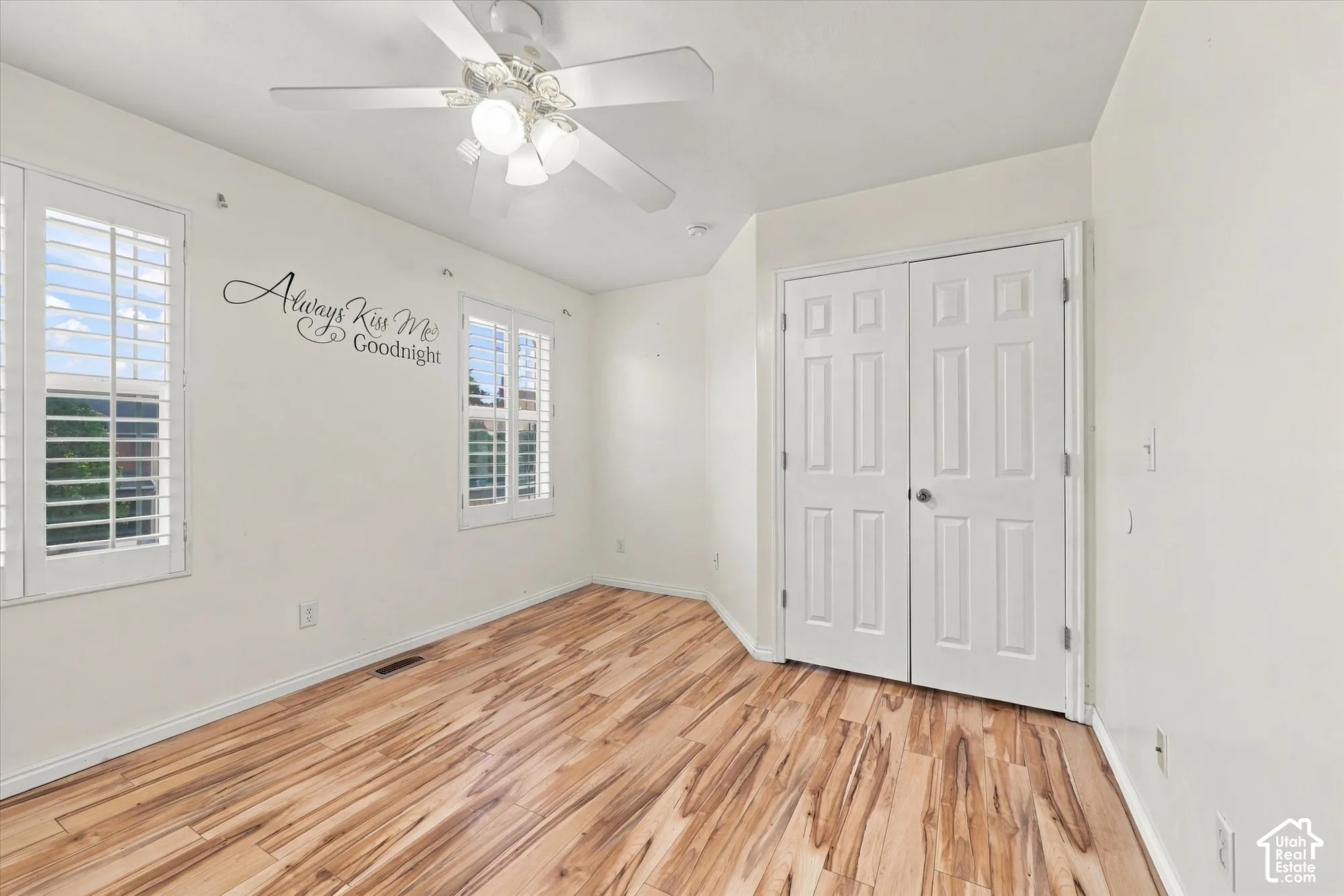 Room featuring wood-finish flooring, white plantation shutters, a dual-door closet, and a multi-bulb ceiling fan