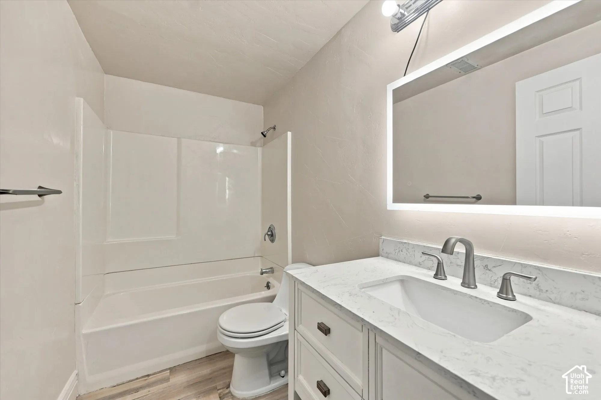 Bathroom featuring a vanity with a stone-finish countertop, undermount sink, integrated LED-backlit mirror, and a tub-shower combination with surround