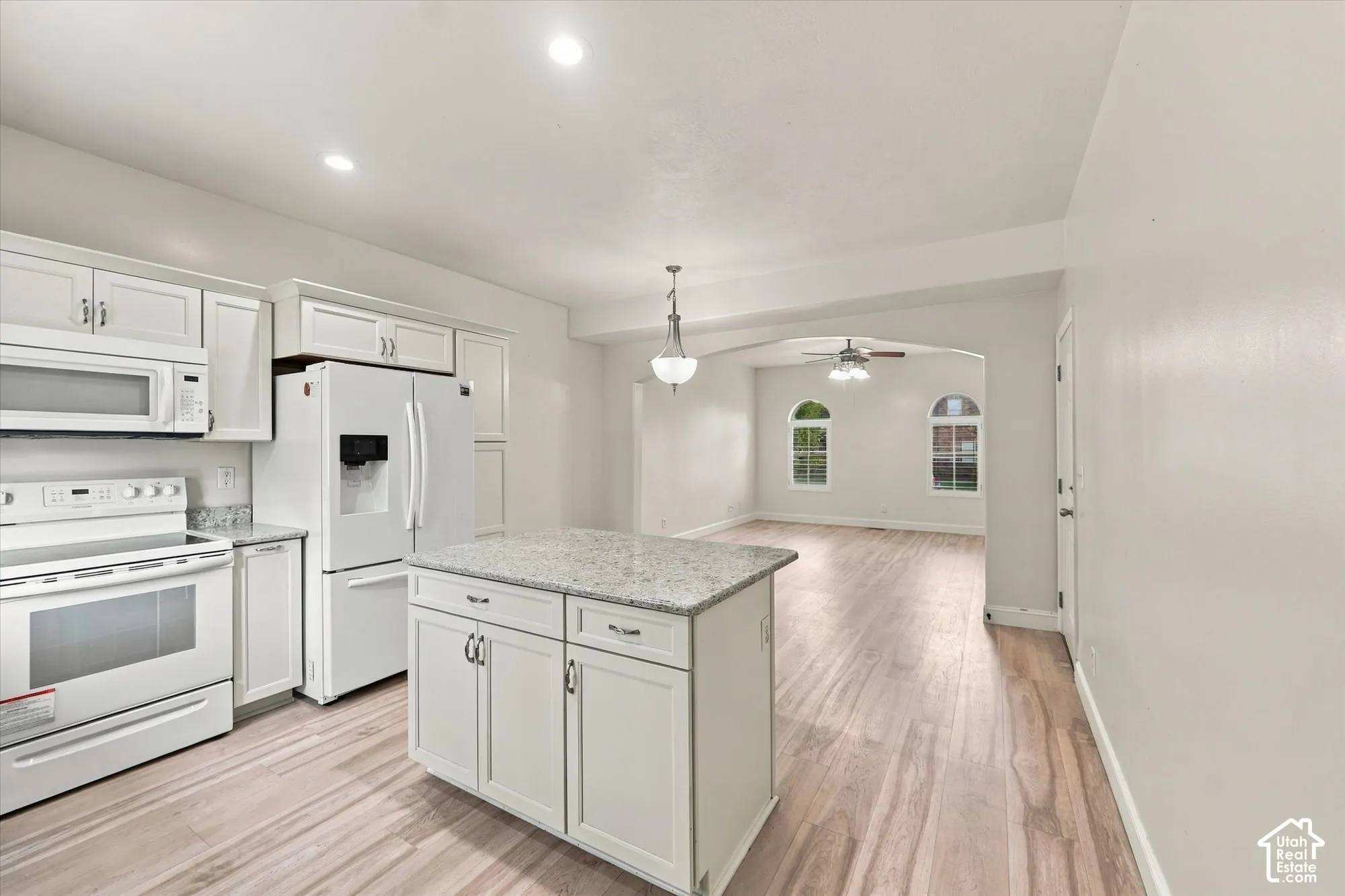 Kitchen featuring white shaker-style cabinetry, stone-surface countertops, central island, wood-finish flooring, and arched window details
