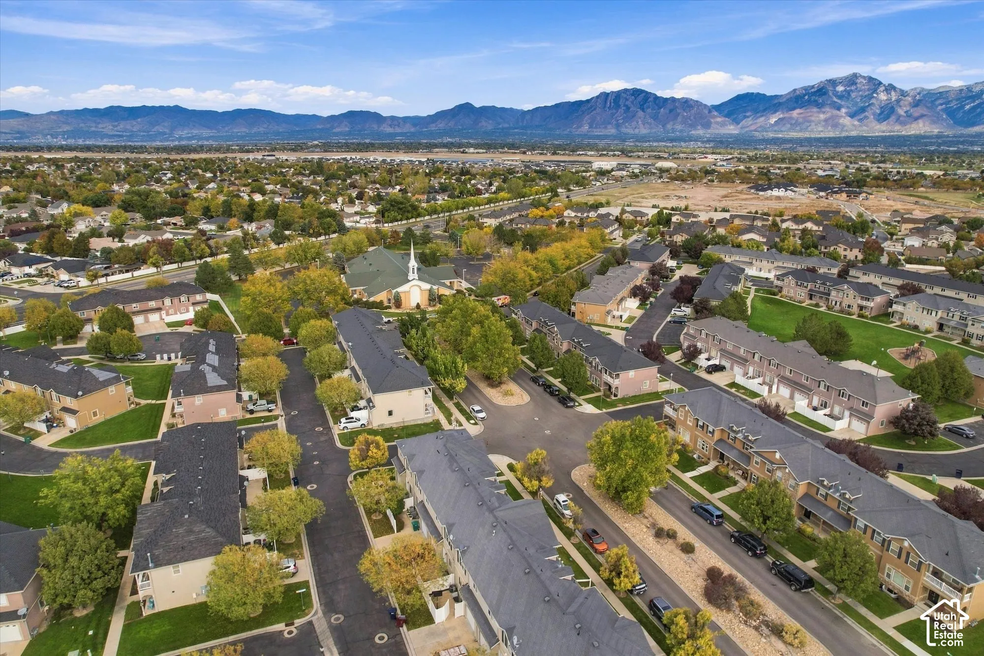 Aerial perspective of a multi-unit residential community featuring asphalt-shingled rooflines, earth-toned masonry exteriors, manicured green spaces, and a mountainous horizon