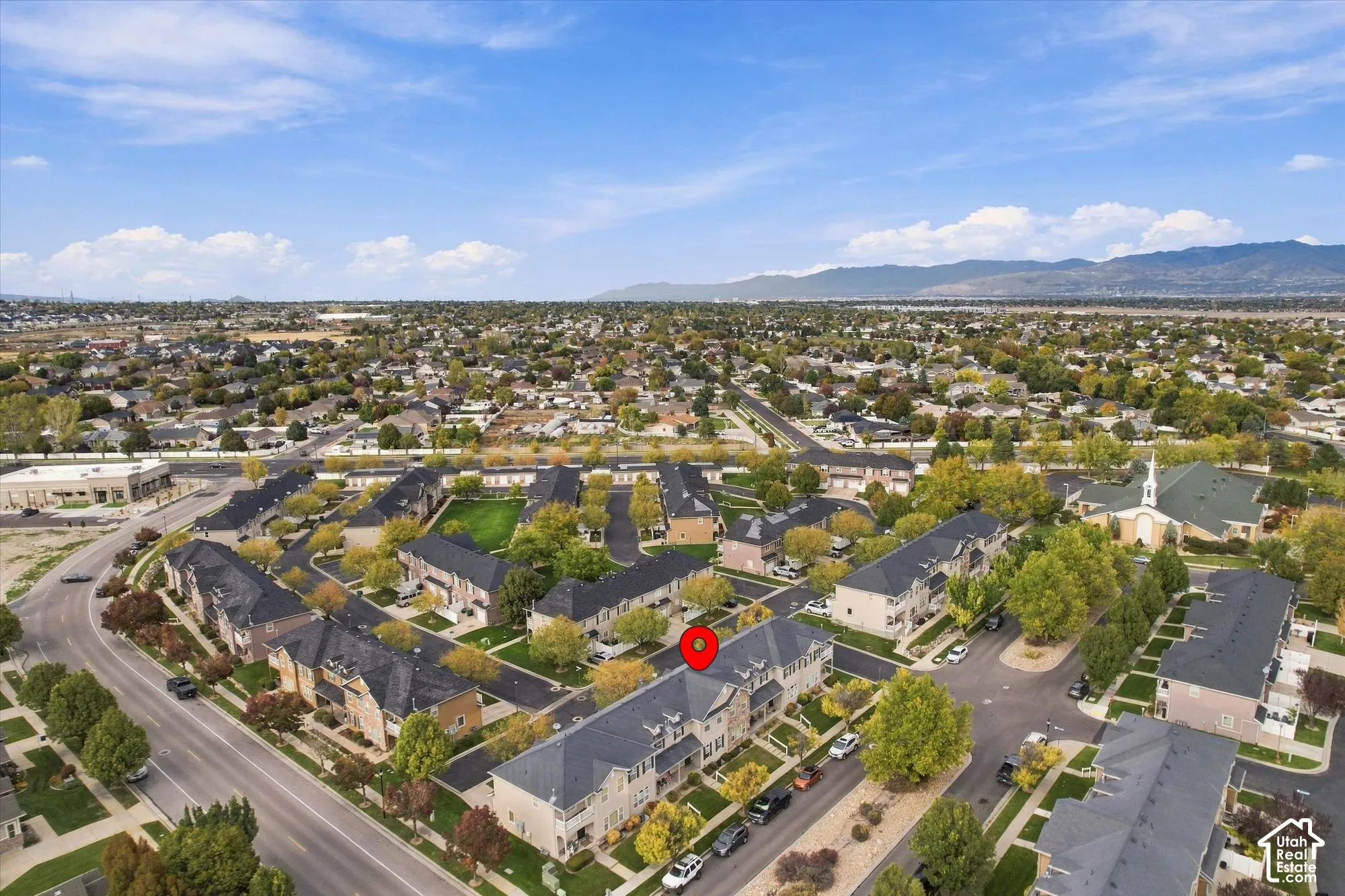 Aerial perspective of a multi-unit property featuring dark-toned roofing, light-colored siding, and proximity to established neighborhood greenery with a backdrop of mountain scenery