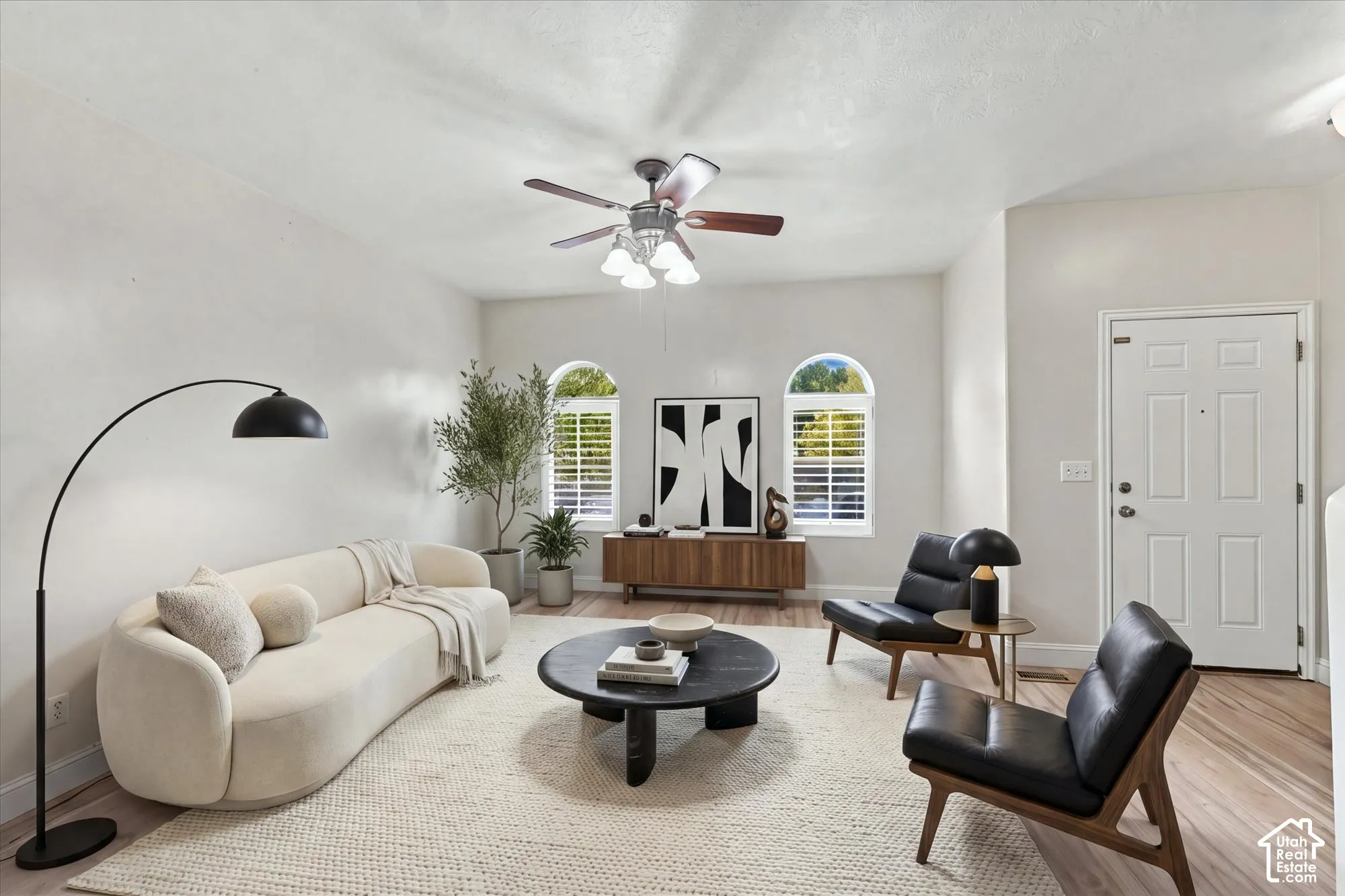 Living area featuring wood-finish flooring, two arched windows with shutter treatments, and a ceiling fan with integrated lighting