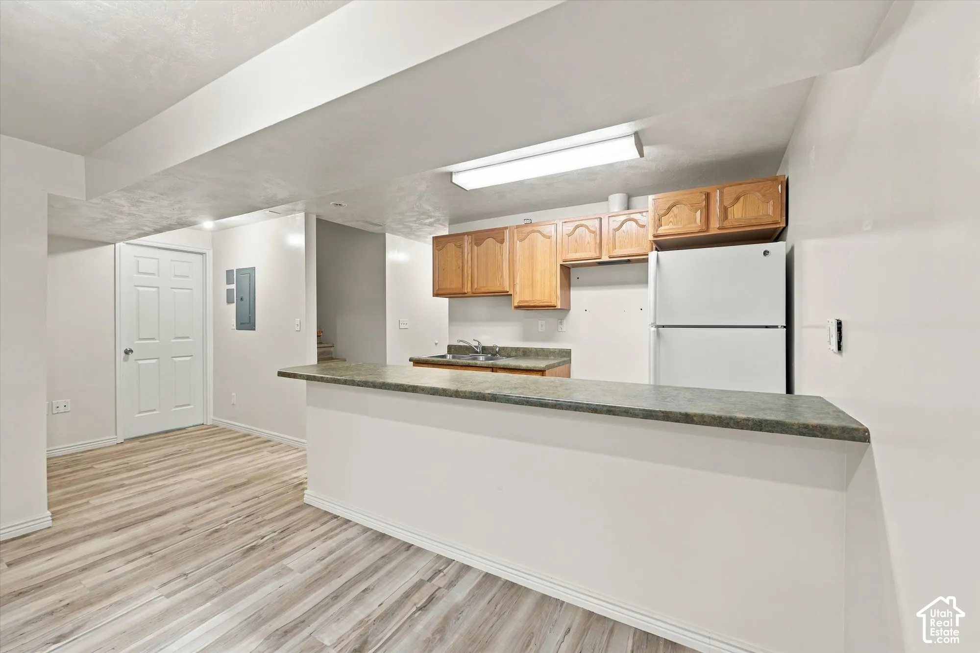 Kitchen area featuring wood-finish flooring, a raised serving counter, natural wood-tone upper cabinetry, and recessed lighting