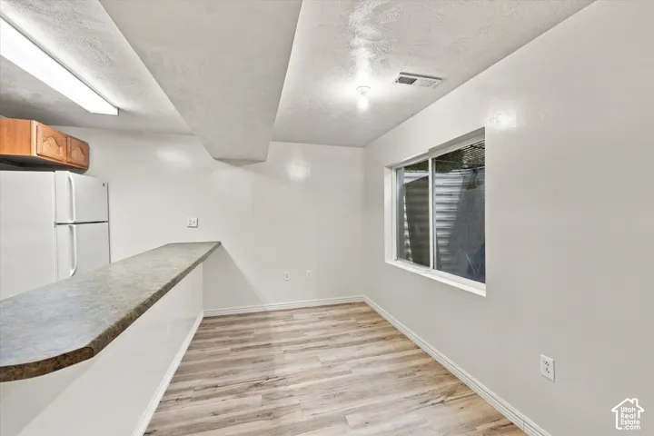 Wood-finish flooring, breakfast bar with solid-surface countertop, ceiling-mounted light fixture, and window with exterior window well