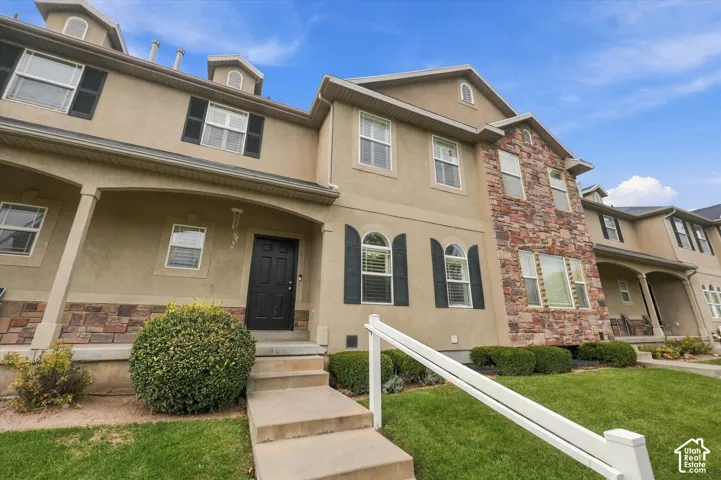 Multi-level exterior featuring stucco siding, stone veneer accents, arched window detailing, shutter accents, and a covered entry porch
