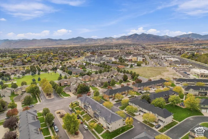 Aerial perspective featuring a multi-unit residential community with paved roadways, managed green spaces, and a mountainous horizon