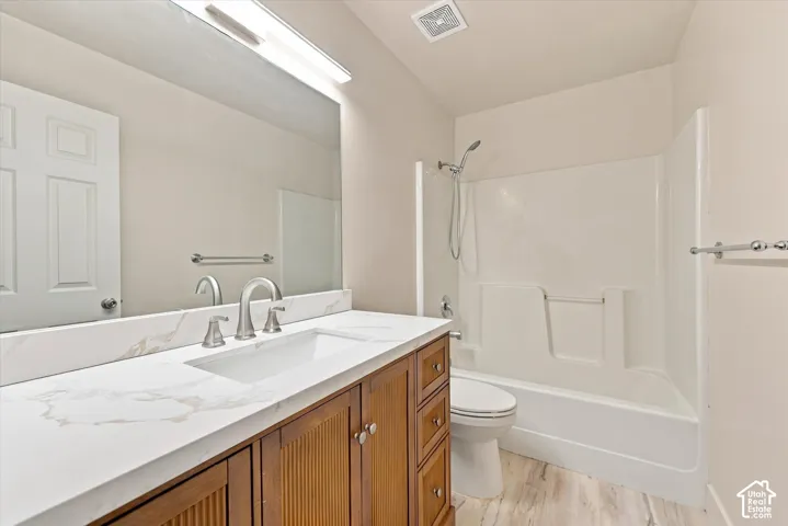 Bathroom featuring wood-finish vanity cabinetry, stone-look countertop with integrated rectangular sink, full-width mirror, brushed nickel faucet hardware, and a tub-shower combination with surround