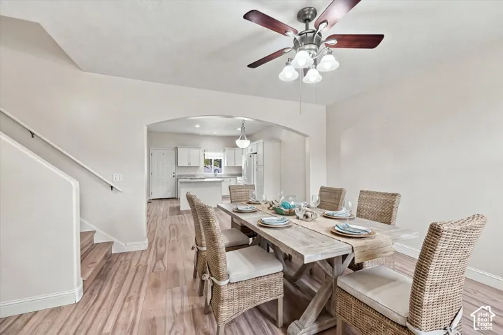 Wood-finish flooring, architectural arched opening, ceiling fan with integrated multi-bulb light fixture, and white cabinetry