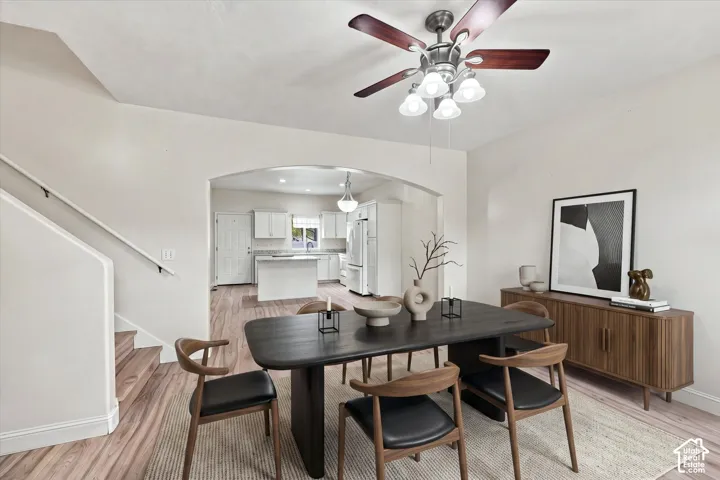 Wood-finish flooring, architectural arched wall opening, multi-blade ceiling fan with integrated lighting, and white cabinetry