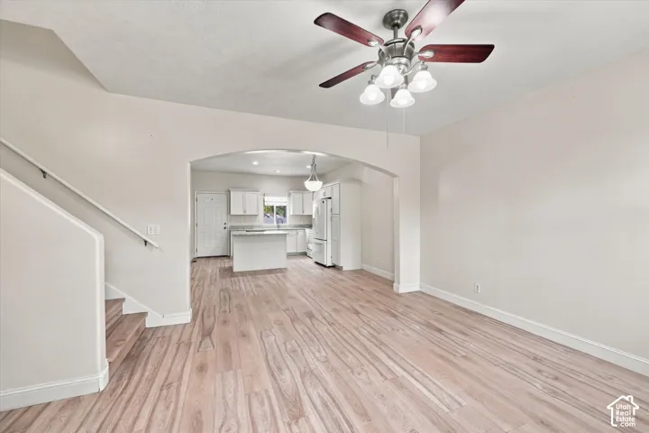 Open-concept interior featuring wood-finish flooring, a vaulted ceiling with a multi-light fan fixture, a prominent architectural archway, and a staircase with a white handrail