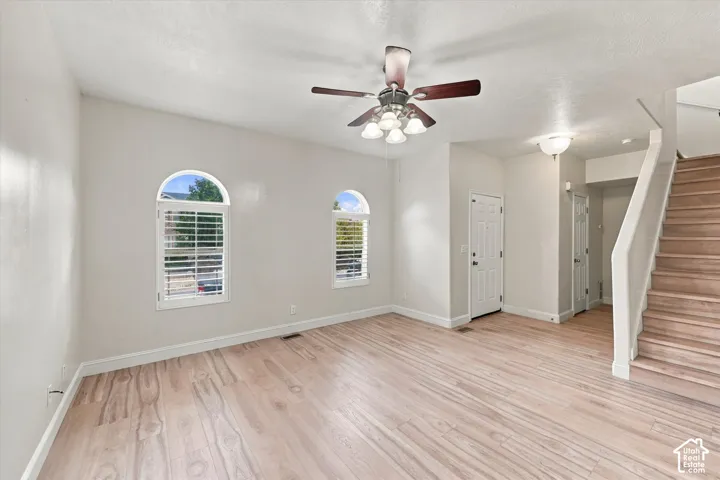Interior space featuring wood-finish flooring, two arched windows with plantation shutters, a ceiling fan with multi-light fixture, and a staircase with wood-finish treads