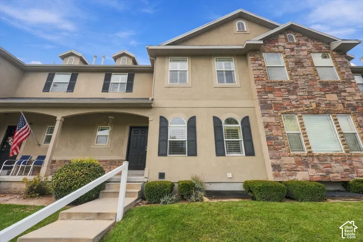 Multi-story stucco and stone veneer exterior featuring arched windows, dark shutters, gabled rooflines, and a covered front porch