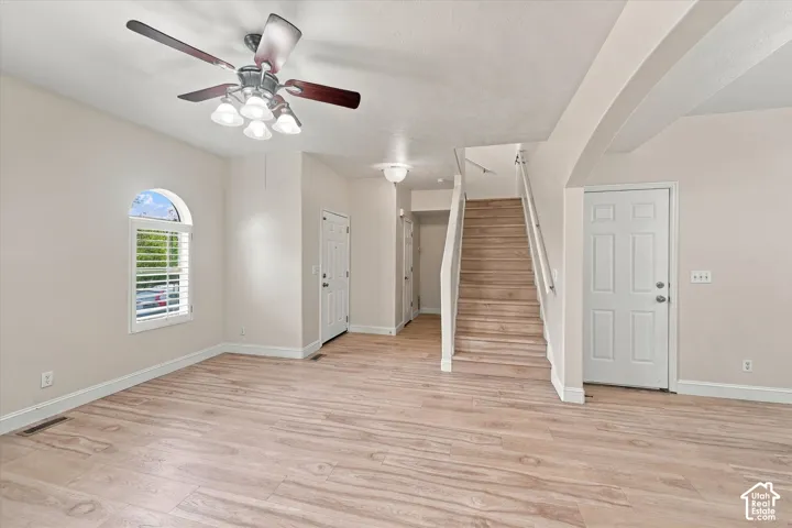 Wood-finish flooring, arched window with plantation shutters, staircase with painted handrail, and multi-light ceiling fan
