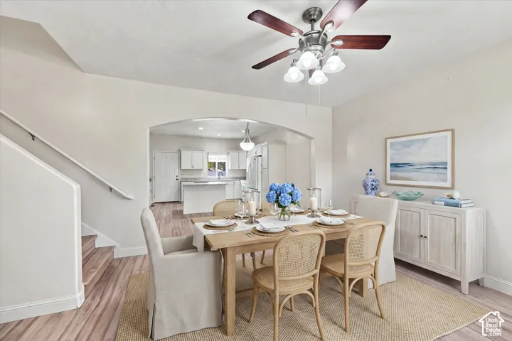 Dining area featuring wood-finish flooring, a neutral color palette, and a multi-bulb ceiling fan with stained wood blades