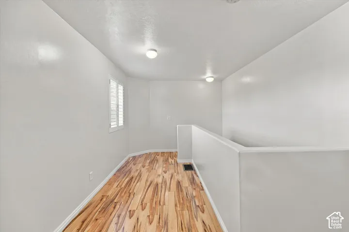 Wood-finish flooring, white walls, dual ceiling-mounted light fixtures, and a single window featuring plantation-style shutters