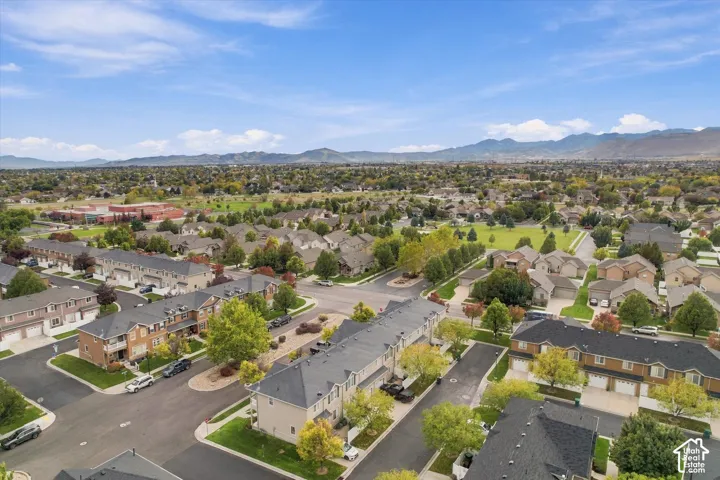 Aerial perspective featuring multi-level residential structures, asphalt roadways, mature deciduous trees, expansive manicured lawns, and a mountain range backdrop