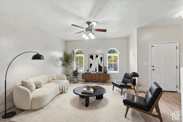 Living area featuring wood-finish flooring, two arched windows with shutter treatments, and a ceiling fan with integrated lighting