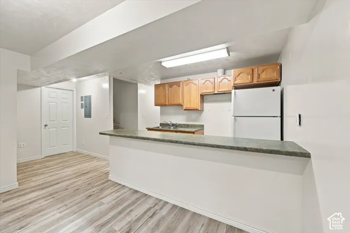 Kitchen area featuring wood-finish flooring, a raised serving counter, natural wood-tone upper cabinetry, and recessed lighting