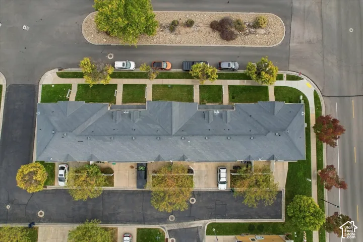 Aerial view of a multi-unit property featuring a shingled gable roof, paved off-street parking, and manicured landscaping