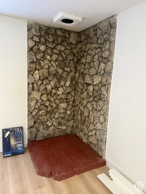 Floor-to-ceiling textured stone accent wall featuring a raised, red brick hearth and neutral wood-finish flooring